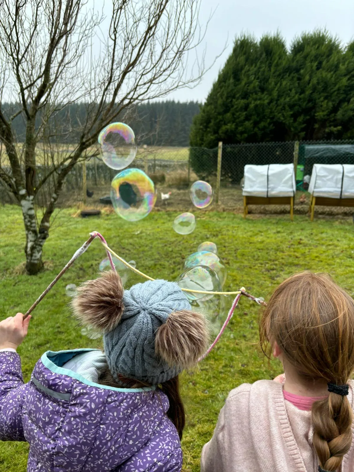 two girls blowing giant bubbles together outdoors