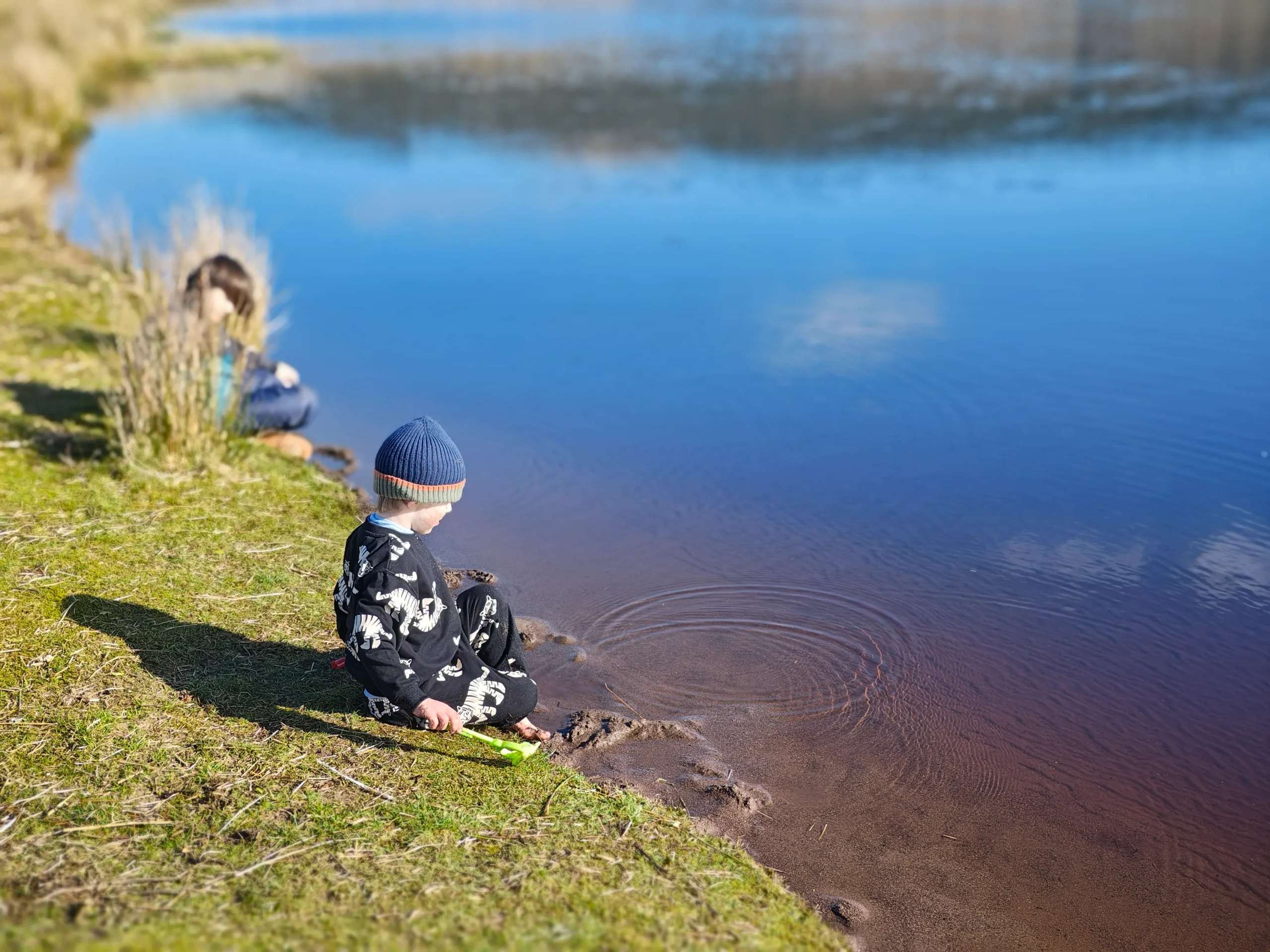 Forest school outdoor learning: children chase giant bubbles by a lake, nature-based play for wellbeing in a small group.